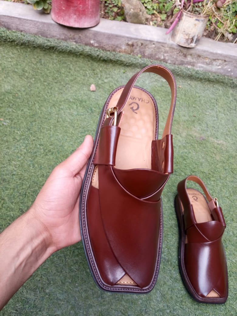 Brown leather sandal held by a hand on a green surface